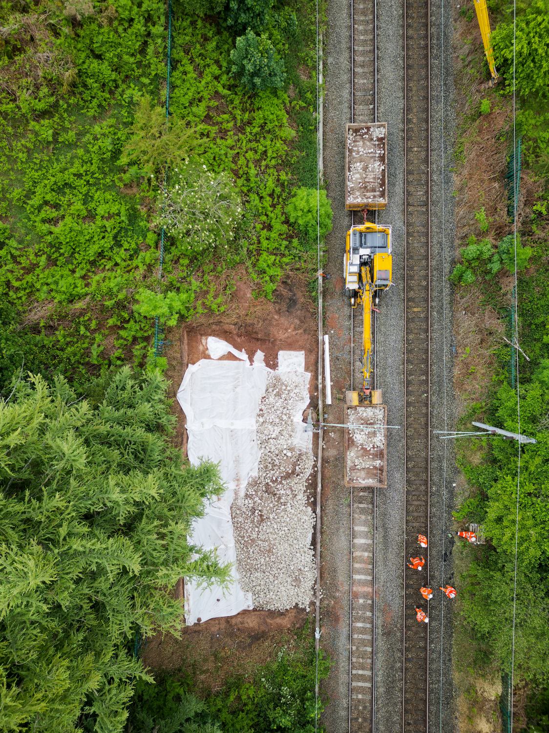 Aerial view of a digger placing aggregate into a geotextile pocket beside the railway